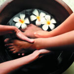 Female feet in foot bath with flowers getting pedicure